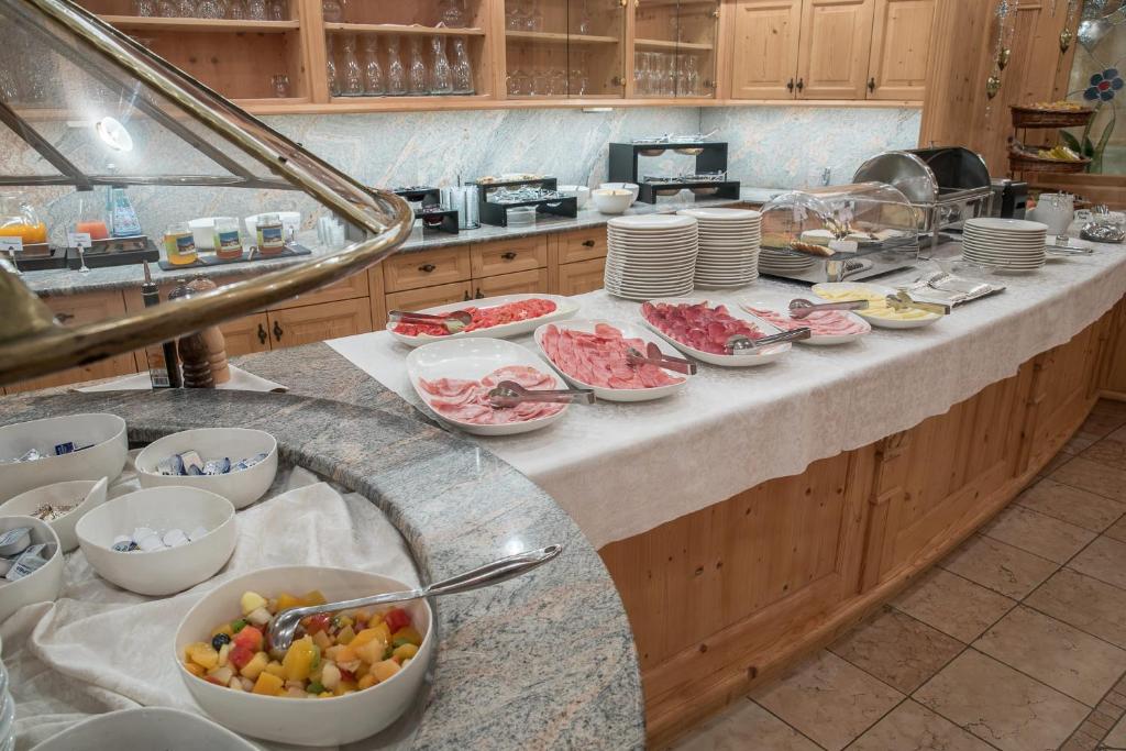 Buffet spread along a wooden counter with plates of sliced meats, bowls of fruit salad, and chafing dishes in a dining area.