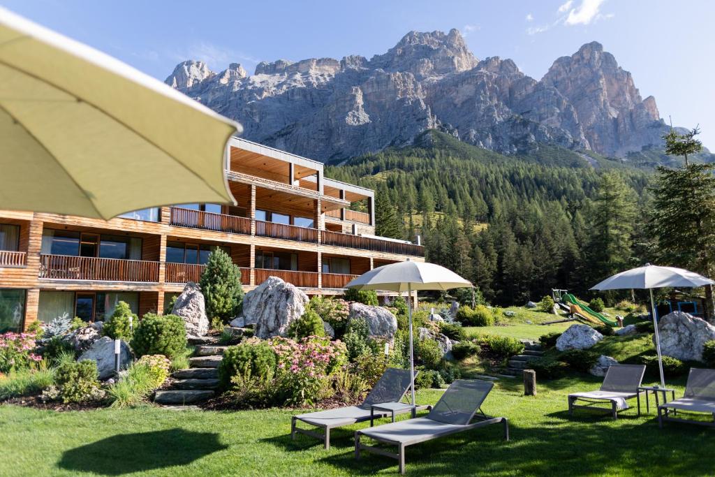 Resort with a multi-level wooden building, balconies, and a rocky, mountainous backdrop; lawn chairs and umbrellas in the foreground.