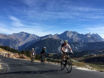 col de la loze-brides les bains - Tour de Vacance Wielervakanties Group of cyclists riding on a mountain road with alpine peaks and blue sky in the background.