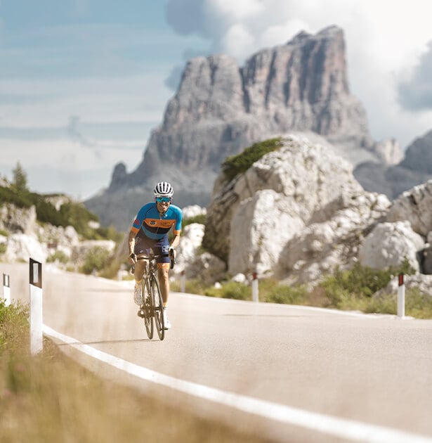 Cyclist in a blue jersey riding a road bike on a mountain pass with rocky cliffs in the background.