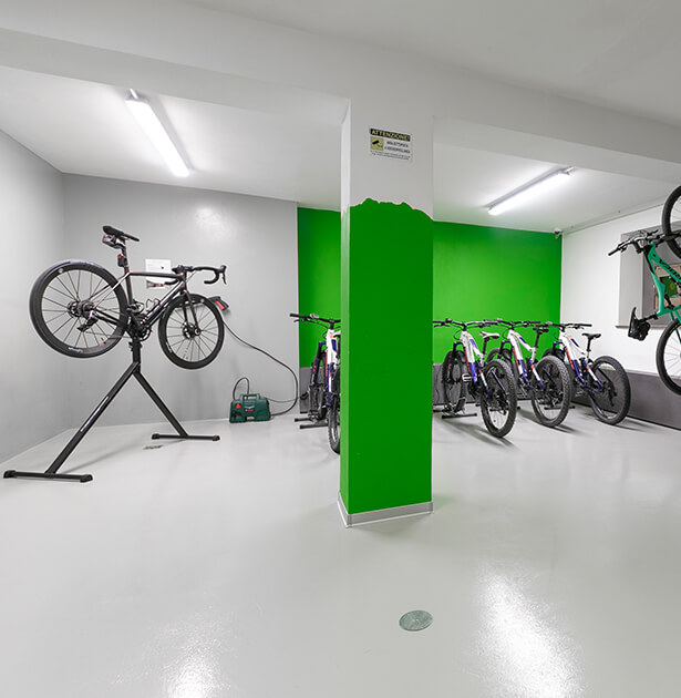 Bike repair workshop with a bicycle on a stand and several bikes parked along a green wall.