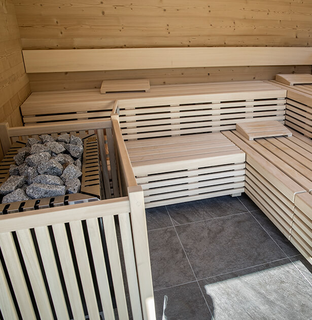 Wood-paneled sauna with tiered benches and a heater filled with rocks in the corner for heat and steam.